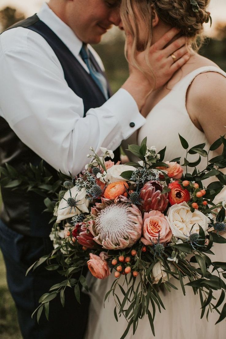 a bride and groom embracing each other in front of the camera with their wedding bouquet