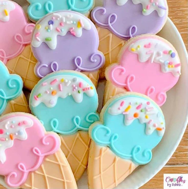 decorated cookies in the shape of ice cream cones on a white plate with pink, blue and purple icing