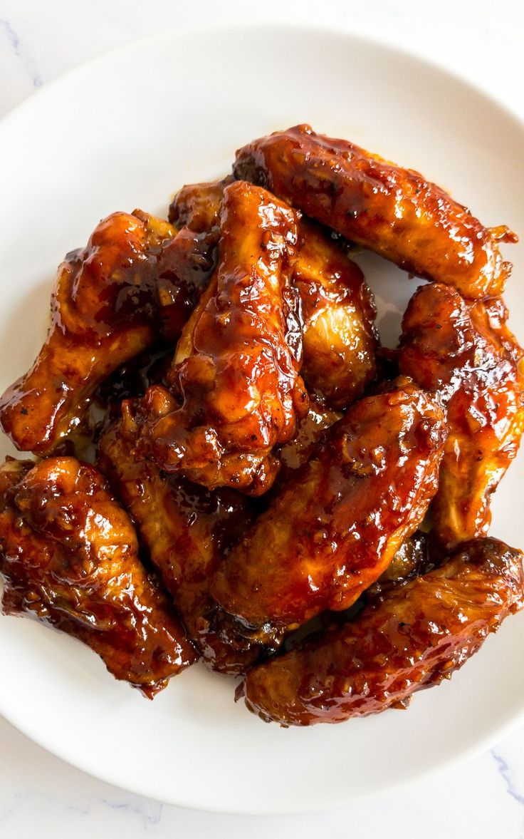 a white plate topped with chicken wings covered in bbq sauce