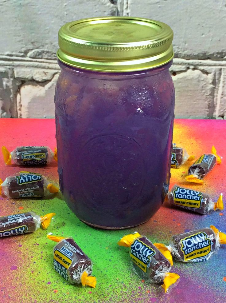 a jar filled with purple liquid next to candy bars on top of a colorful table