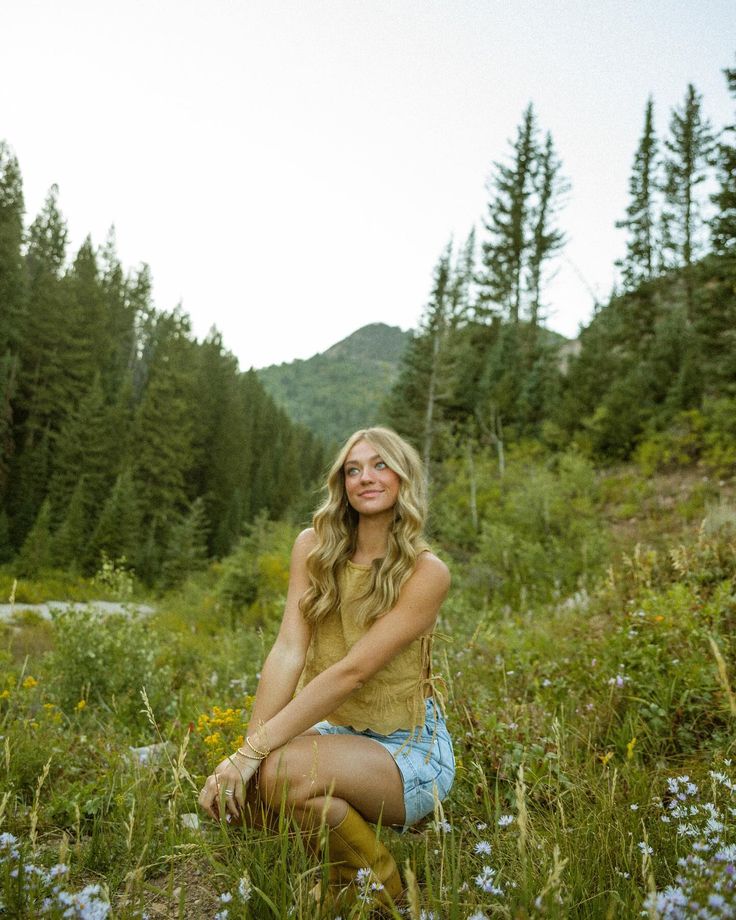 a woman is sitting in the middle of a field with wildflowers and trees