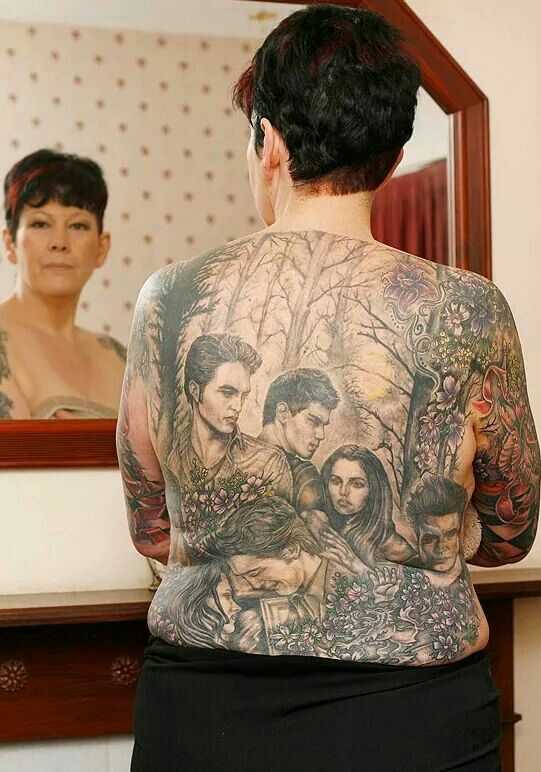 the back of a man with tattoos in front of a mirror and another woman behind him