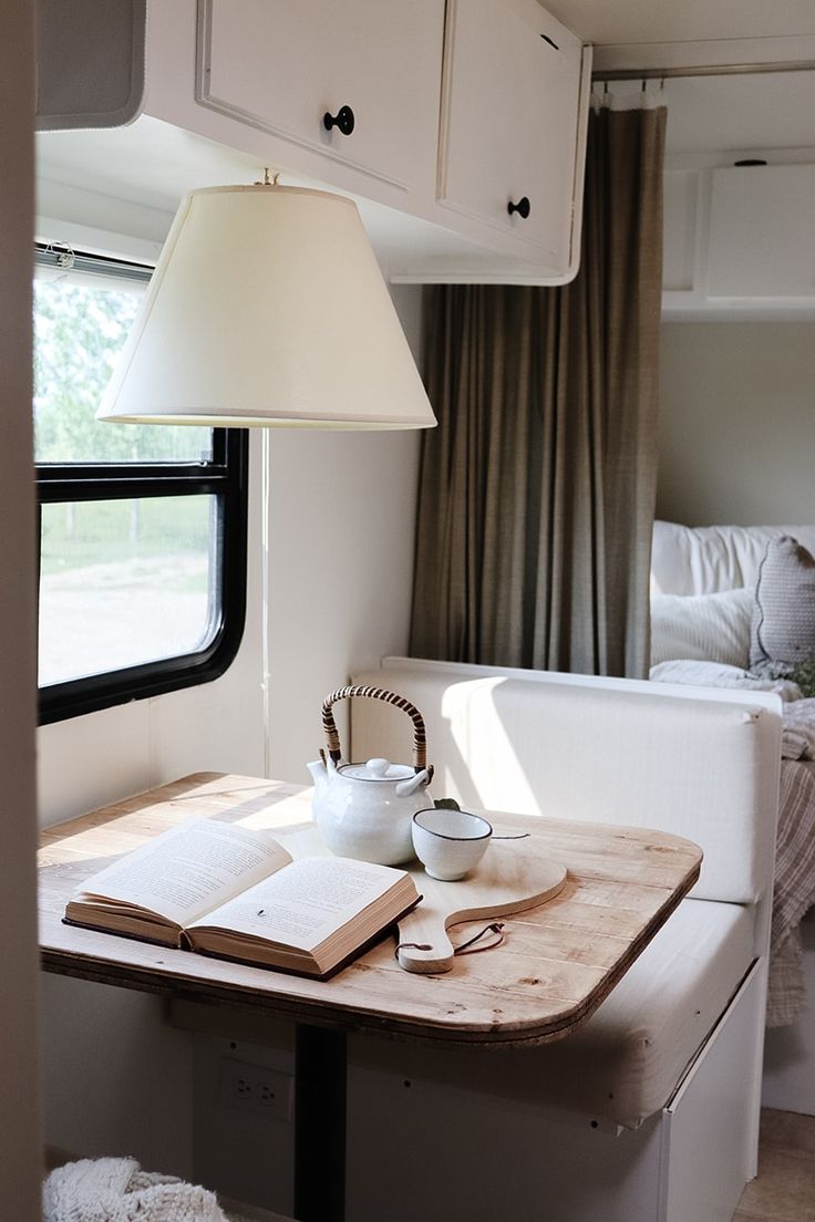 a table with a book, tea pot and cup on it in front of a window