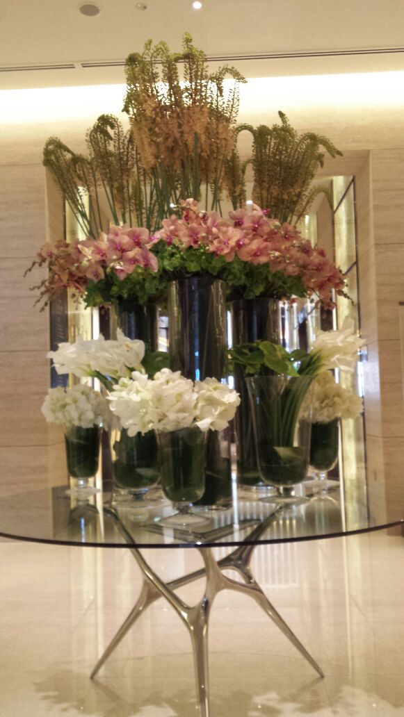 vases filled with flowers sit on a glass table in front of a large mirror