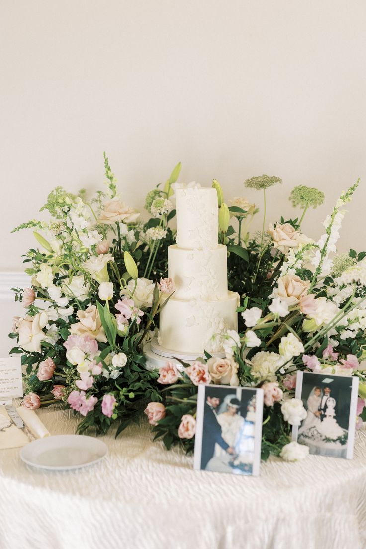 a white wedding cake sitting on top of a table next to pictures and flowers in vases