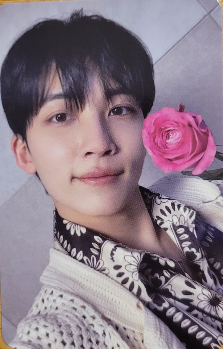 a young man holding a pink rose up to his face and looking at the camera