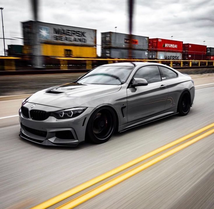 a silver car driving down the road with cargo in the backgrouds behind it