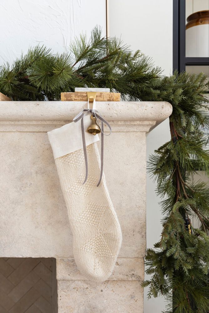 a white christmas stocking hanging from a fireplace mantel with pine needles and greenery