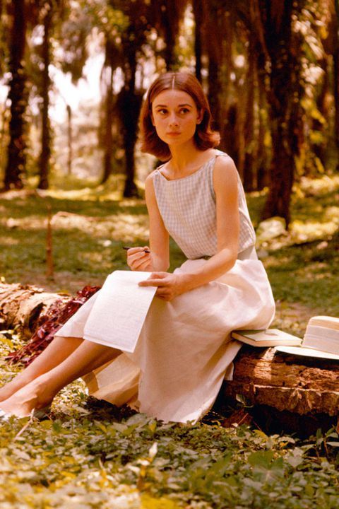 a woman is sitting on a log in the woods with her hat and book open