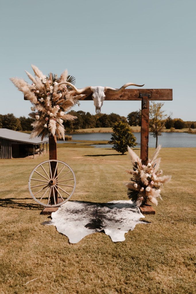 an outdoor ceremony setup with flowers, feathers and a wagon on the grass in front of a lake