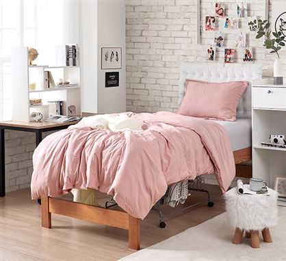 a bed with pink comforter and pillows in a room next to a white brick wall