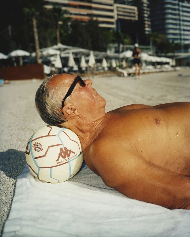 an older man laying on the beach with a soccer ball