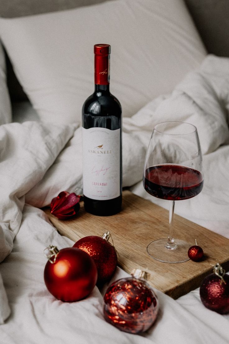 a bottle of wine and two ornaments on a bed next to a glass of red wine