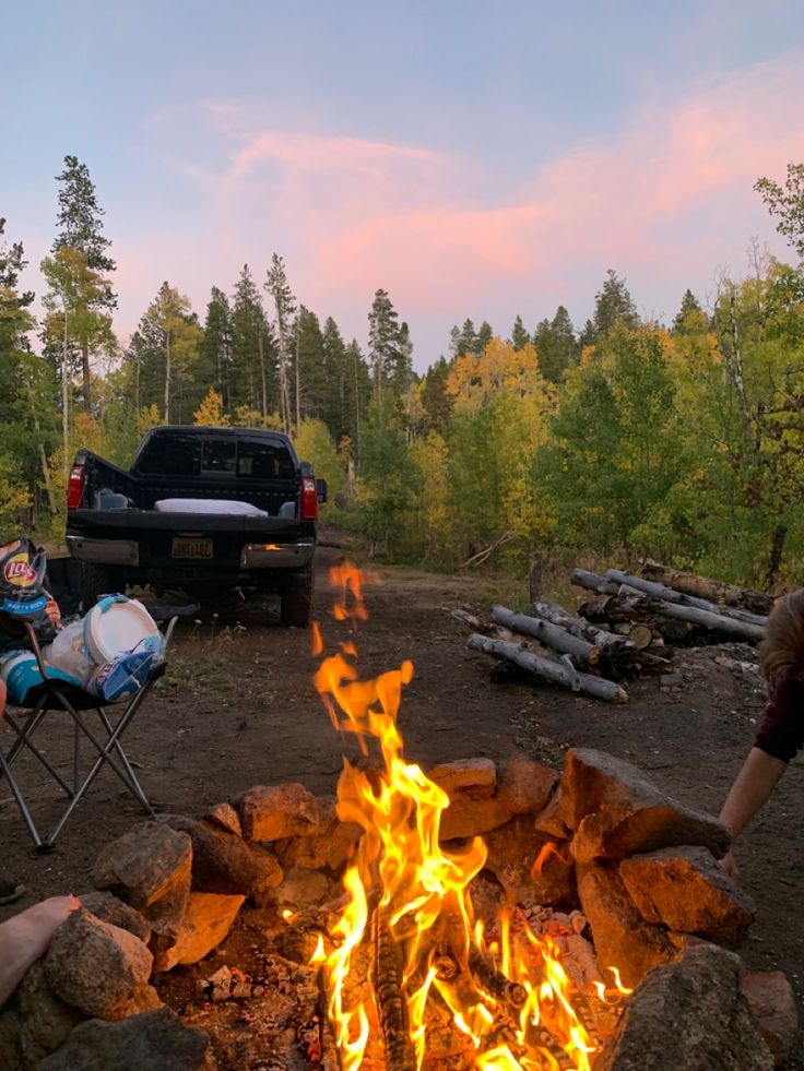 two people sitting in chairs around a campfire with the sun setting on it's side