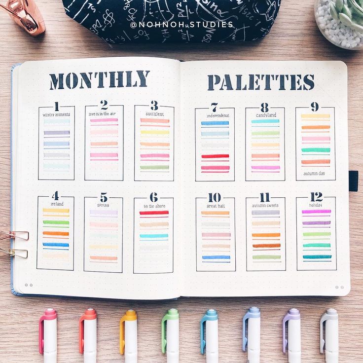 an open planner sitting on top of a wooden table next to pens and pencils