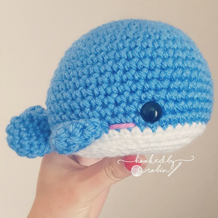 a crocheted blue and white whale hat is held up in the air by someone's hand