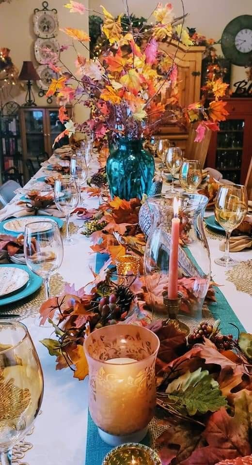 a table set for thanksgiving dinner with plates and glasses on it, surrounded by fall leaves