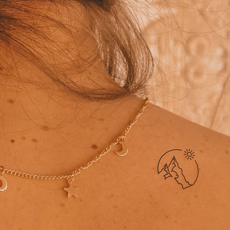 the back of a woman's neck with gold chains and stars attached to it