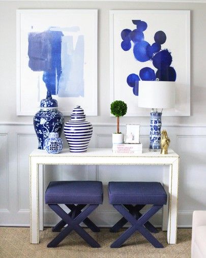 two blue and white vases sitting on top of a table in front of paintings