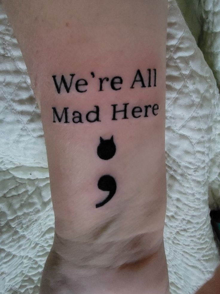 we're all mad here tattoo on the arm with a black cat in it