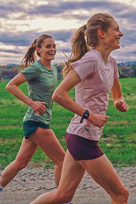 two women running in a race with grass and sky in the backgrouds