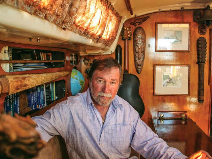 a man sitting at a table in front of a book shelf filled with books and other items