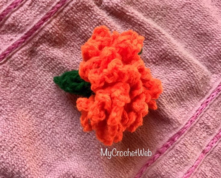 an orange crocheted flower sitting on top of a pink blanket