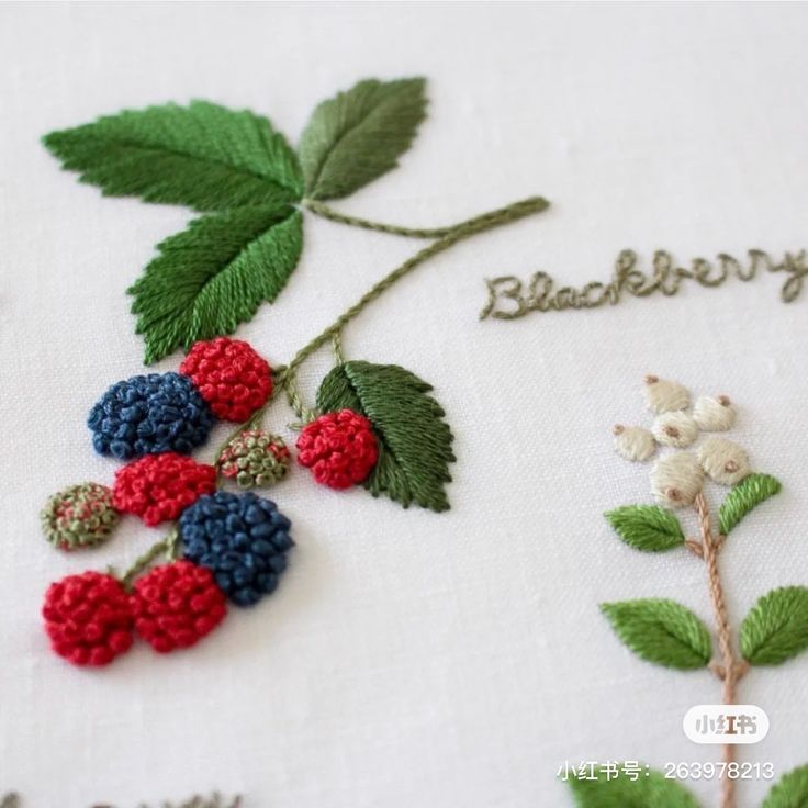 a close up of a piece of embroidery with berries and leaves on it, next to another piece of thread