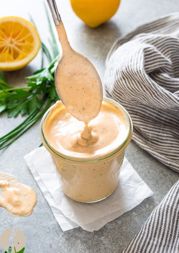 a spoon full of dressing being poured into a glass jar with oranges in the background