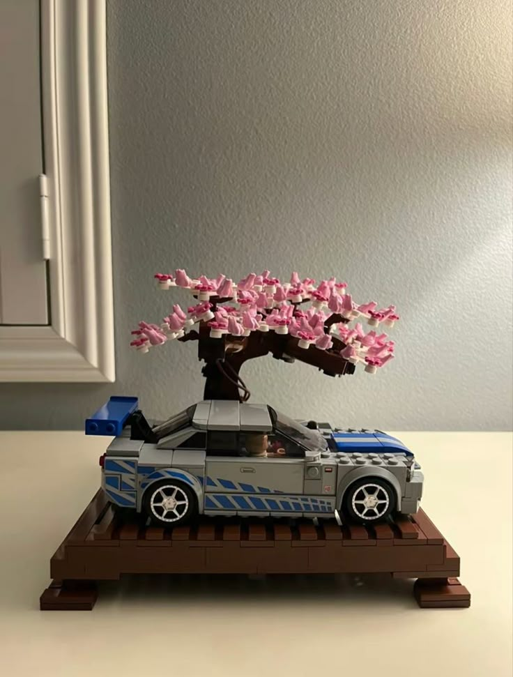 a lego car is parked under a tree with pink flowers in the trunk on a table