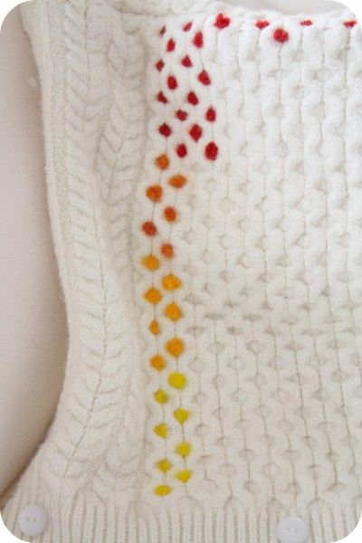 a white knitted blanket with red, yellow and orange dots on the bottom half