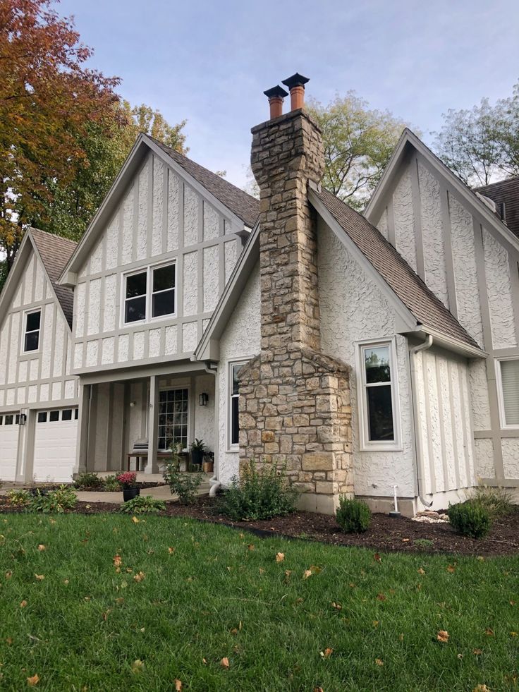 a white house with two story windows and a brick chimney in the middle of it's front yard