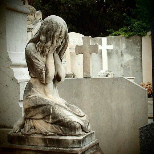 an old statue sitting on top of a cement slab next to a cemetery with tombstones