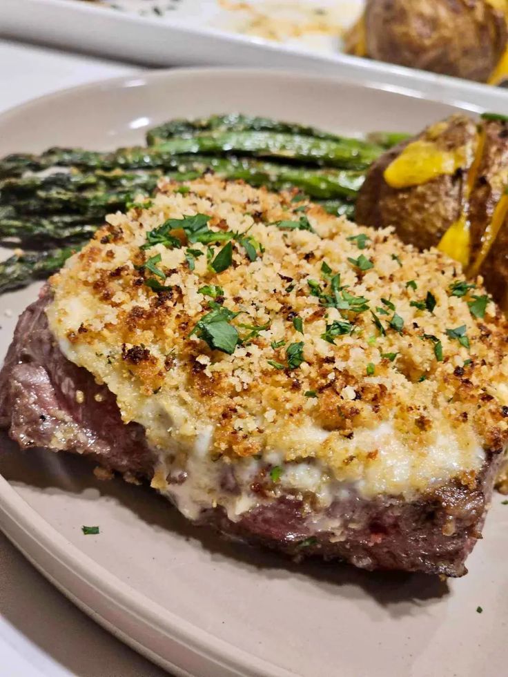 a white plate topped with steak and asparagus next to potatoes on a table