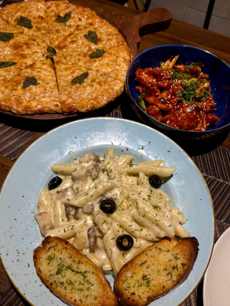 two plates of food on a table with one pizza and the other pasta dish next to it