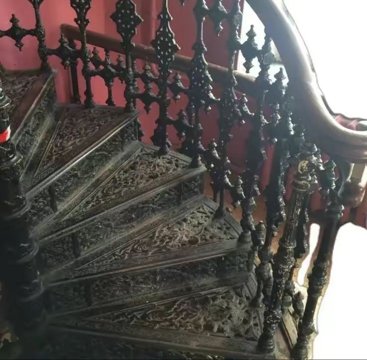 an old wooden staircase with wrought iron handrails and red wall in the background