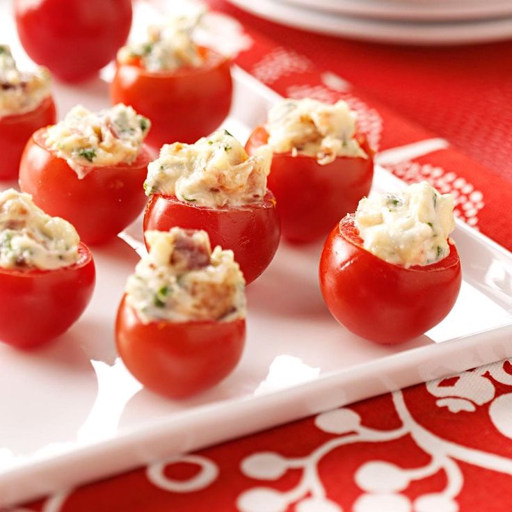 small tomatoes stuffed with crab salad on a white plate next to a red and white table cloth