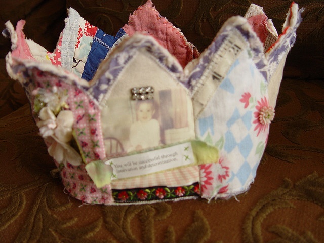 a small crown made out of fabric with pictures on the front and sides, sitting on a couch