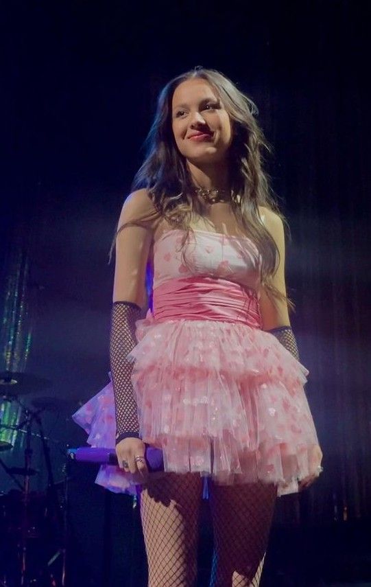 a woman in a pink dress is standing on stage with her legs crossed and wearing fishnet stockings