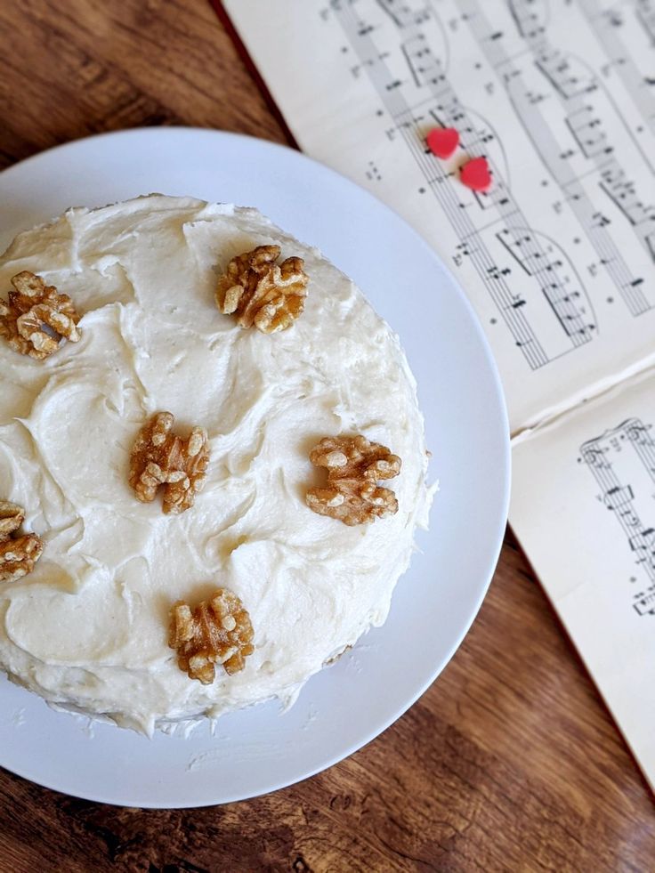 a cake with white frosting and walnuts sitting on top of a wooden table