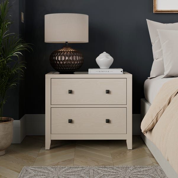 a nightstand with a lamp on top of it next to a bed and a rug