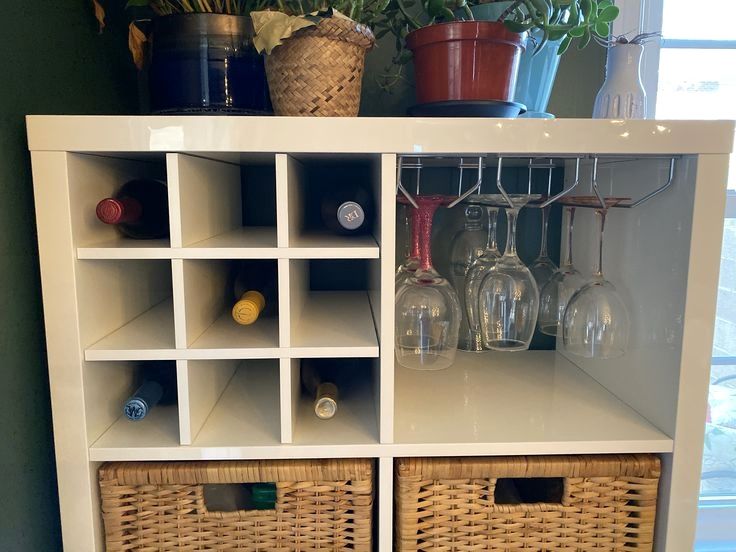 a white shelf with wine glasses and bottles on it next to a potted plant