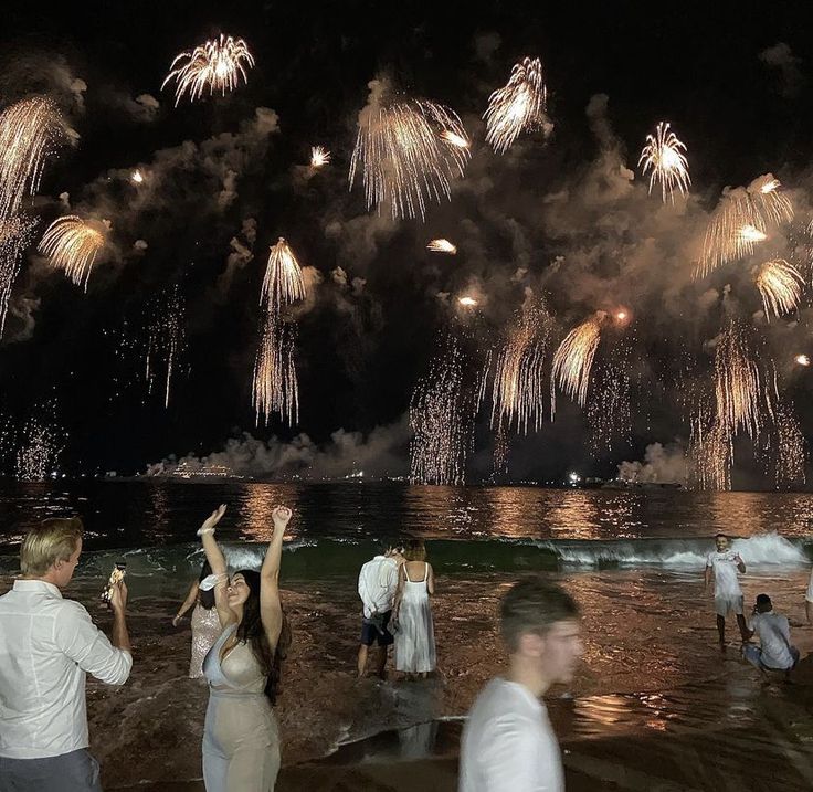 people are standing in the water watching fireworks