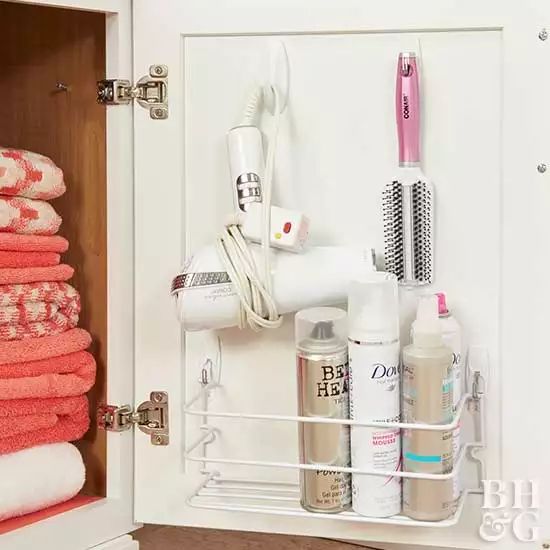 an organized bathroom cabinet with pink towels and hairdryers on the door, along with other personal care items