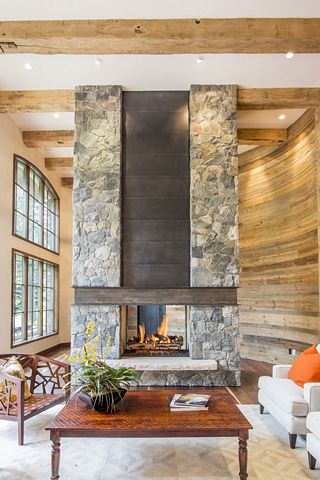 a living room with couches and a fireplace in the center, surrounded by wood paneled walls