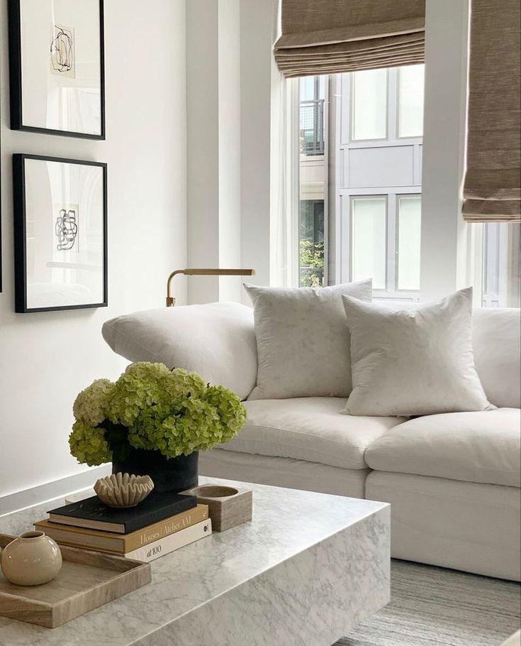 a living room with white couches and pictures on the wall above it, along with a marble coffee table