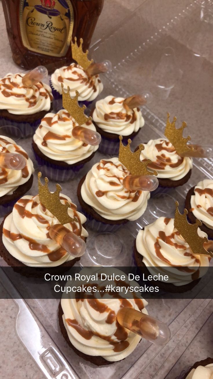 cupcakes with frosting and gold crown decorations on top are sitting in a plastic tray