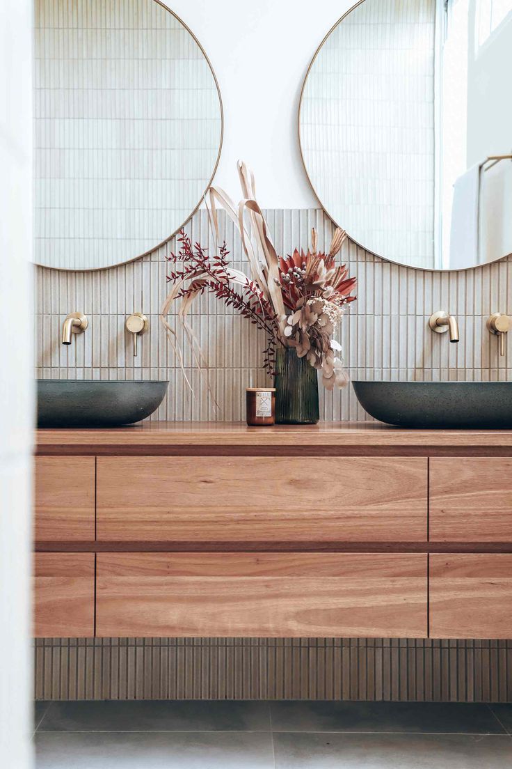 two round mirrors are above the double sinks in this bathroom with wood cabinetry and marble countertops