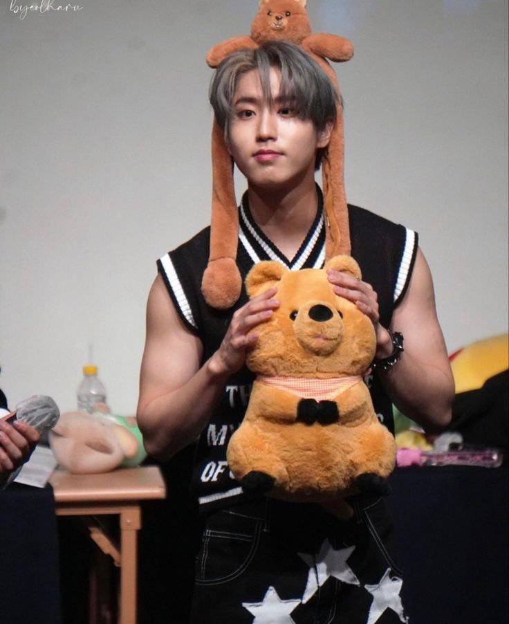 a young man holding a teddy bear in his hands and wearing a hat on top of his head