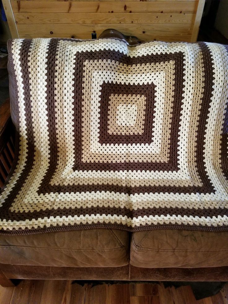 a brown and white crocheted blanket sitting on top of a leather couch next to a wooden wall